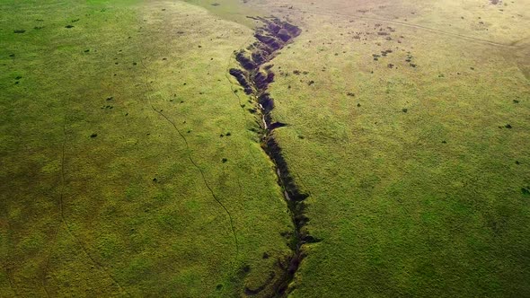 Creek runs through green fields and reveal of sunrise over distant hills alt