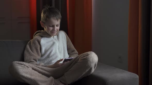 Boy with Smartphone in Hands Sits on Sofa. Quarantine 2020