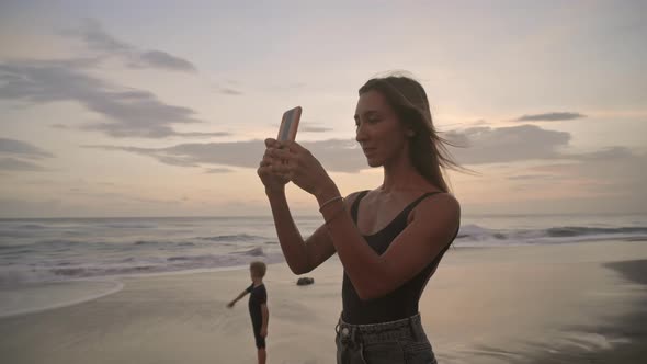 Woman Taking Photos of Sunset at Beach alt