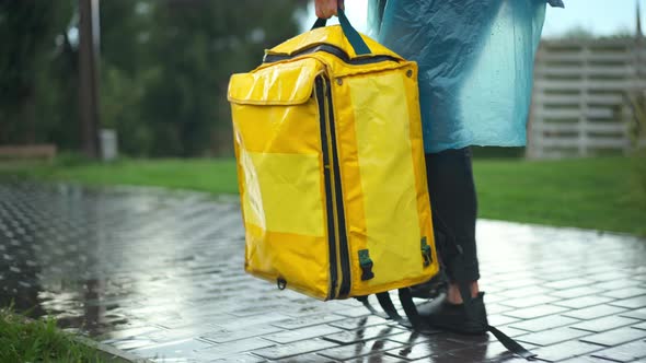 Tracking Shot of Yellow Delivery Bag in Hand of Unrecognizable Courier in Rain Coat Walking in Urban alt