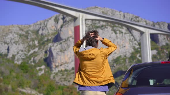 A Man Standing By His Car Looks at the Moracica Bridge in Montenegro alt