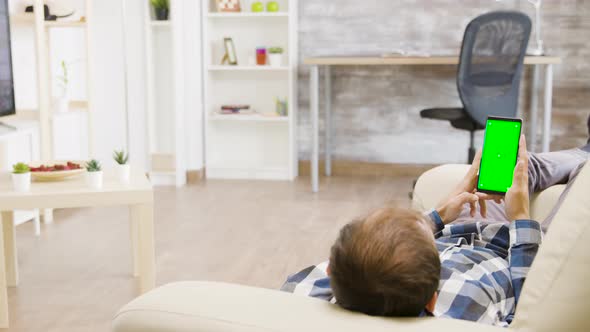 Parallax Shot of Male Lying on the Sofa and Looking at Green Screen Phone alt