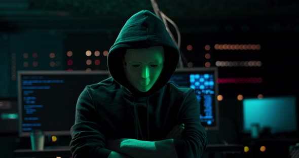 Dangerous Internationally Wanted Hacker with Masked Face Speaks Into the Camera In the Background alt