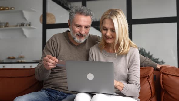 Cheerful Middleaged Couple Watching at Laptop Screen and Checking Credit Card Number alt