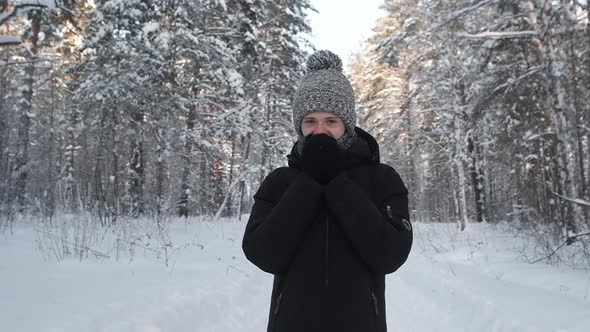 Portrait young man in knitted hat and mittens warms face. Frosty day in forest alt