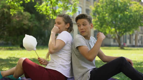 Funny Teens Sitting Back To Back And Fooling Around While Eating Cotton