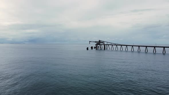 Old abandon coal loading dock protruding out above a moody sky ocean. Moving drone view alt