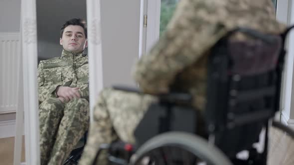 Reflection in Mirror of Young Paraplegic Man in Wheelchair Adjusting Camouflage alt
