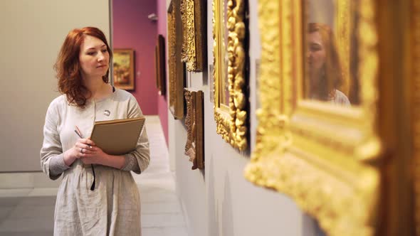 Woman in Grey Dress Walks Along Paintings in Golden Frames