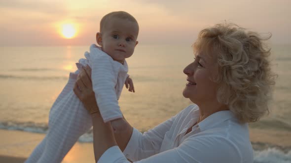 Happy Grandmother Holding Her Granddaughter in Her Arms By the Sea