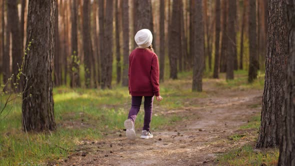 The Little Girl Runs Along the Path Road in the Pine Forest. Dressed in the Leather Jacket