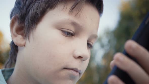 Teenager Playing Video Games on His Smartphone Outdoors alt