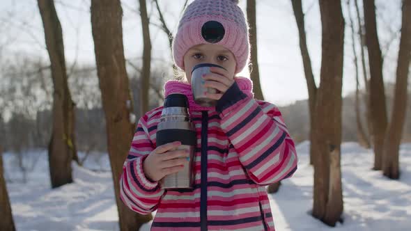 Portrait of Cute Smiling Child Girl Kid Traveler Walking Drinking Hot Drink Tea in Winter Park alt