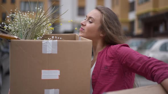 Portrait of Young Caucasian Brunette Woman with Heavy Boxes Outdoors on Parking Lot at Residential alt