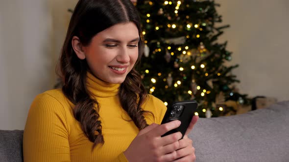 Smiling Woman Buys New Year Gifts on Internet Using Smartphone Christmas Tree alt