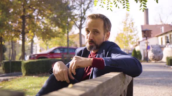 A Middleaged Handsome Caucasian Man Talks to the Camera with a Smile As He Sits on a Bench