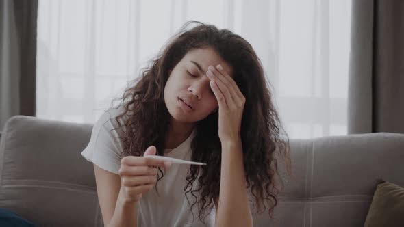 Sick Young African American Woman Checking Body Temperature Holding and Looking at Thermometer alt