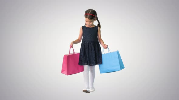 Beautiful Little Girl in Black Dress Walking with Shopping Bags on Gradient Background. alt