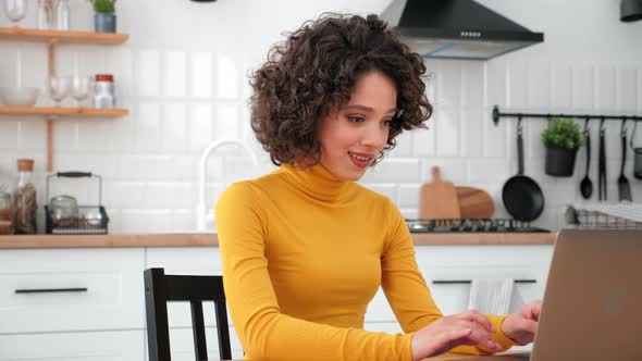 Smiling Woman Student Studying Uses Laptop Typing on Keyboard at Home Kitchen alt