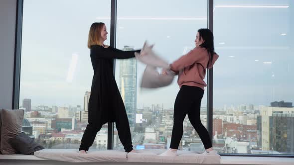 Two Girlfriends Staged a Pillow Fight Standing on the Windowsill