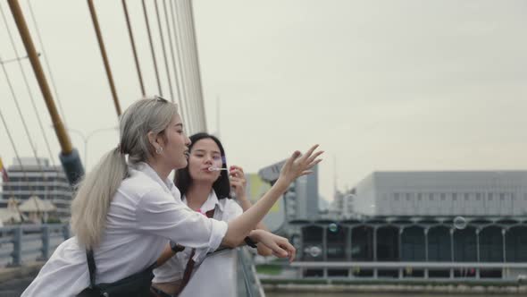 Asian lesbian couples playing soap bubbles while standing on the bridge.