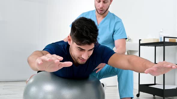 Physiotherapist Helps Handsome Young Patient for Doing Pilates Exercises with Ball alt