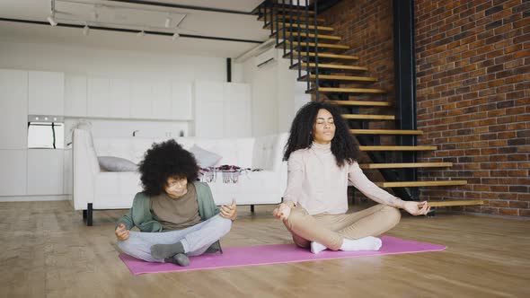 African American Young Mother Meditates in the Lotus Position alt