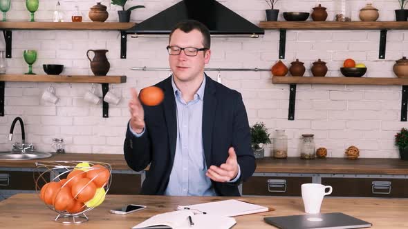 Relaxed Male Entrepreneur in Business Suit and Glasses Tosses an Orange From Hand to Hand While
