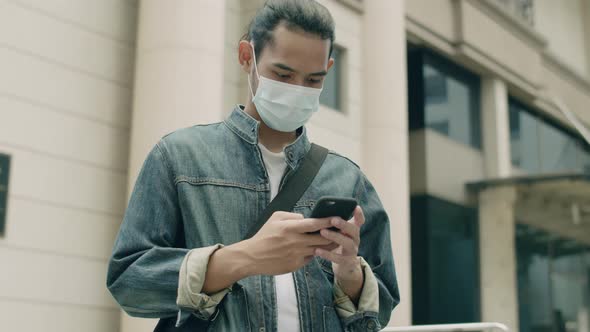 Handsome Asian man wearing a surgical mask and using smartphone.