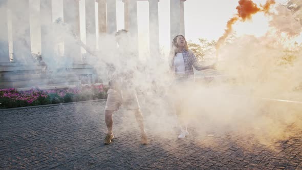 African American Girl and Guy Dancing in Park Against Columns and Waving Colorful Smoke Bombs alt