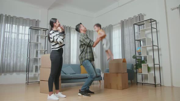 A Happy Wife Looking Her Husband Holding A Son Up In The Air To Celebrate Moving Day In A New House alt