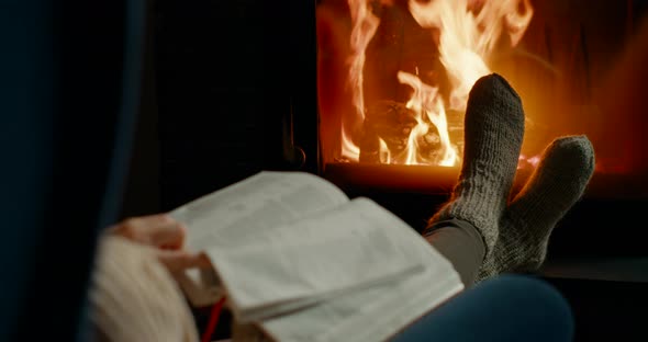 Christian Woman Opens and Reads Holy Bible By Fireplace in Cozy Room at Night