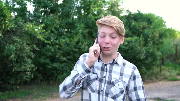 Young Caucasian Teenager Man in a Light Gray Checkered Shirt Speaks on the Phone alt