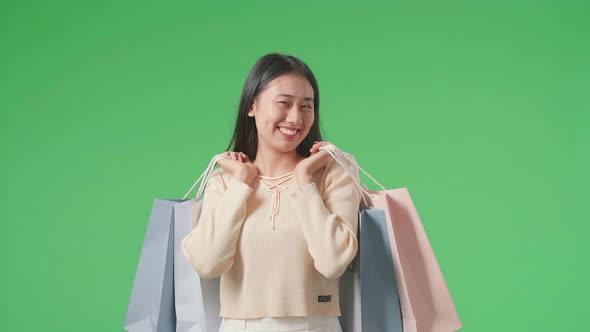An Asian Shopping Woman Holding Shopping Bags Smile And Walking In Front Of Green Screen alt