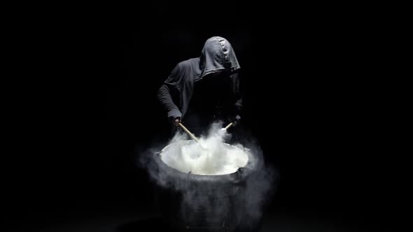 Hooded Man Beats Drum with Flour alt