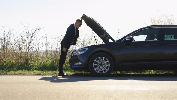 Disappointed Mature Man in Formal Outfit Opening Bonnet of Broke Down Car to Check Engine alt