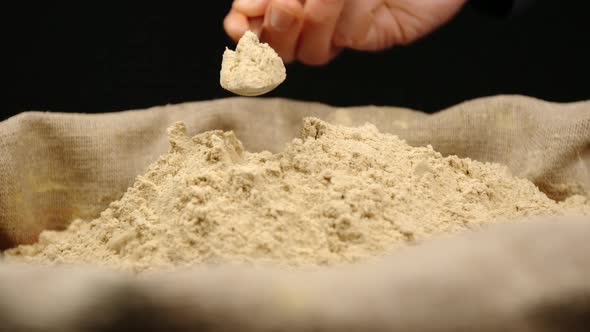 Human hand takes a pinch of a ginger powder by a spoon from a top of pile in a sac