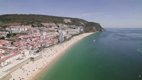 Seagulls flying above the ocean, Sesimbra sand beach and cityscape against hills. Aerial view alt