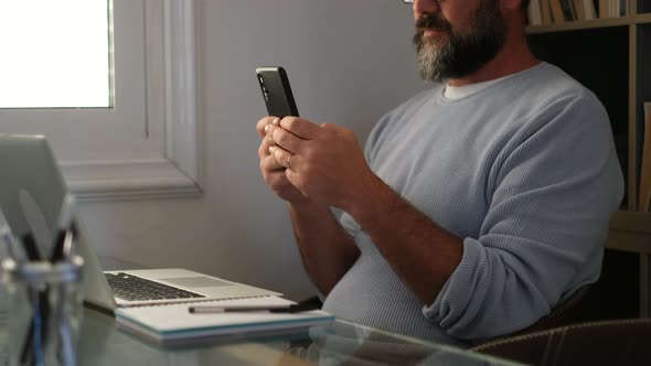 Businessman in home office text messaging on smartphone