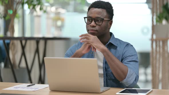 Young African Man Thinking While Using Laptop in Modern Office alt