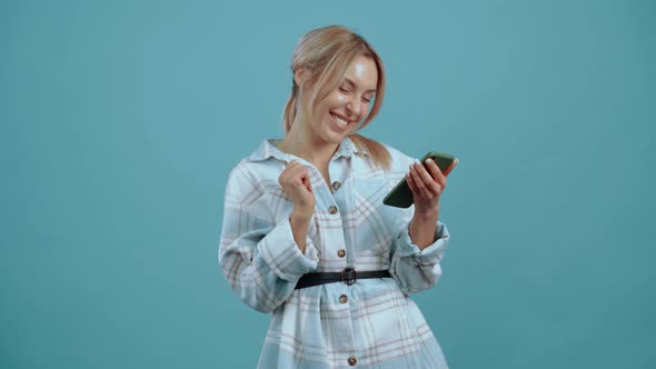 The Young Woman is in a Good Mood with Her Phone in Her Hand She Smiles Excitedly at the Room alt