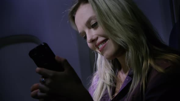 Closeup of young woman using cell phone at night on airplane
