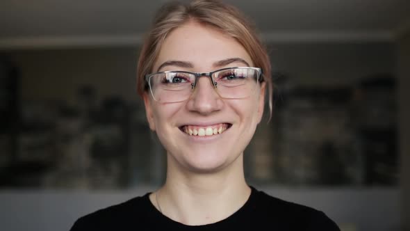 Close-up portrait of smiling woman with glasses looking at camera at home