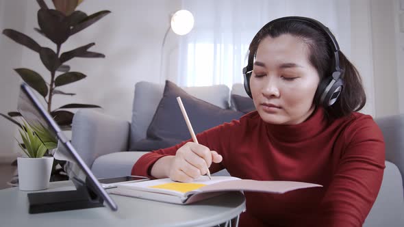 Businesswoman redshirt using a tablet with headphone for meeting online at home alt