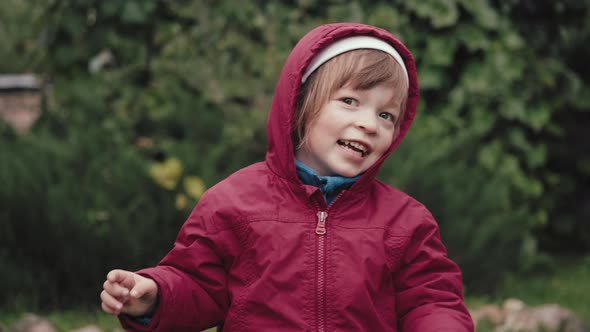 Cute Little Girl in a Hooded Jacket is Happy and Makes Faces in Front of Camera
