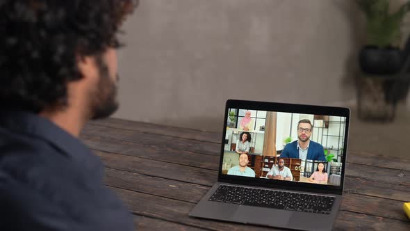Young Guy Relaxed Sitting at the Table and Talking Online Via Video Call with Group