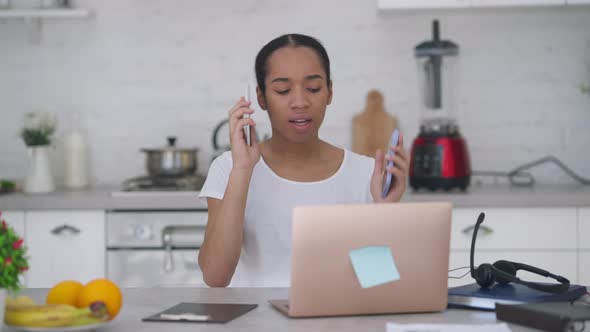 Overburdened Young Slim Woman Talking Using Two Phones Typing on Laptop Keyboard alt