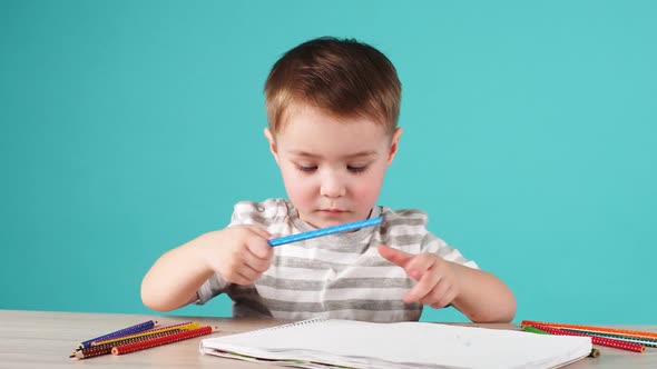 Young Talented Boy Draws a Pencil Drawing in Album on Blue Background. alt