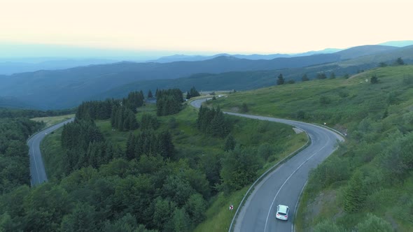 Drone Follwoing Two Cars on Curvy Mountain Pass Road with Green Valley Below alt