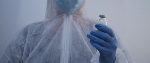 Person holding a vaccine bottle with blue gloves left to right slow motion